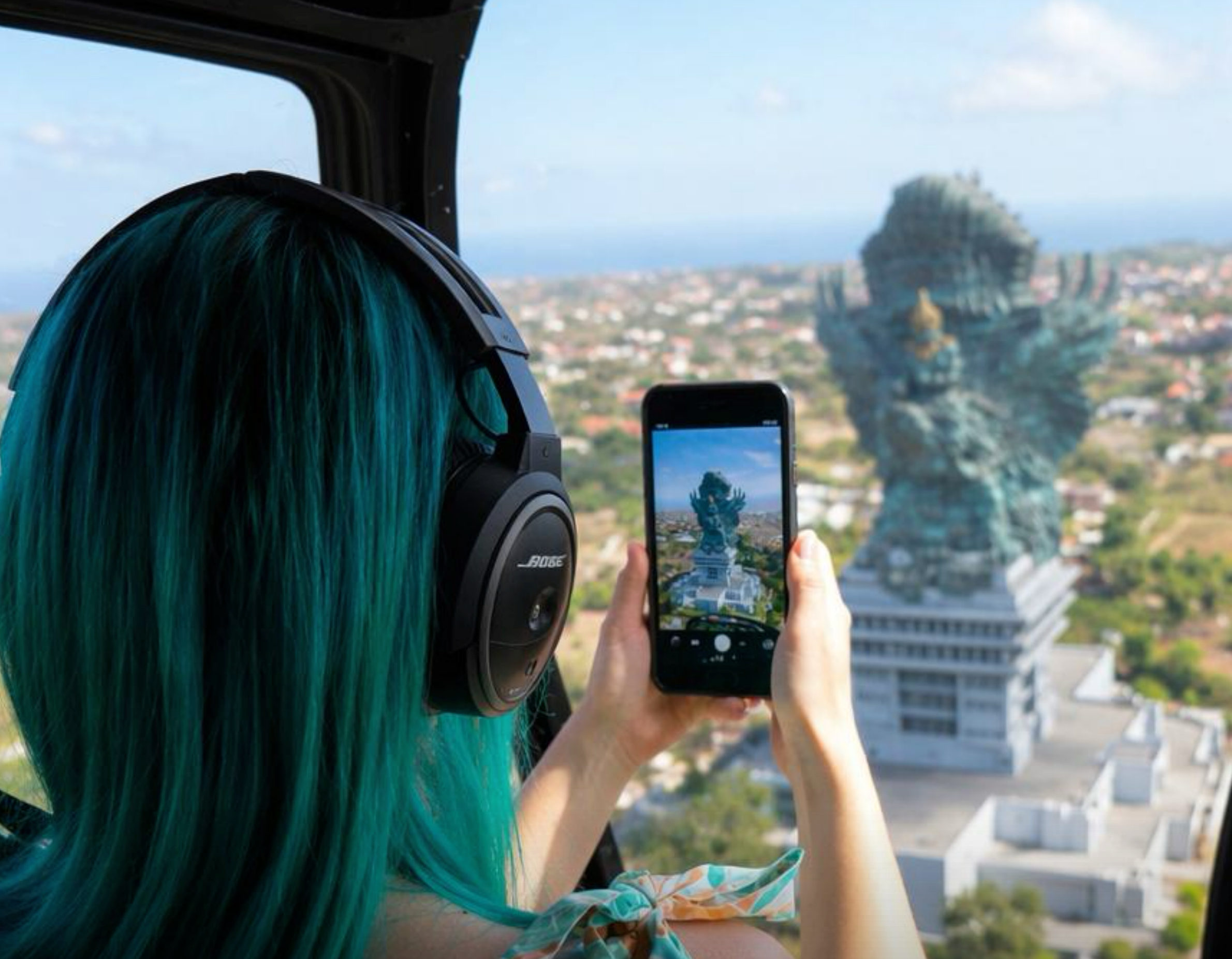 Passenger photographing the Garuda Wisnu Kencana statue from a helicopter cabin above the Bukit peninsula